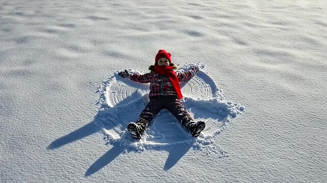 Child making snow angel in winter.