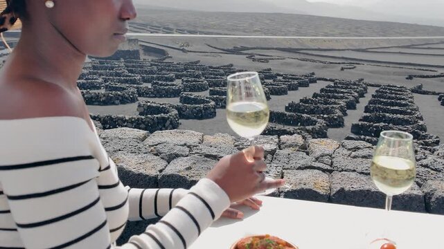 Unrecognizable female traveler tasting a glass of local Malvasia white wine at a vineyard in La Geria, Lanzarote