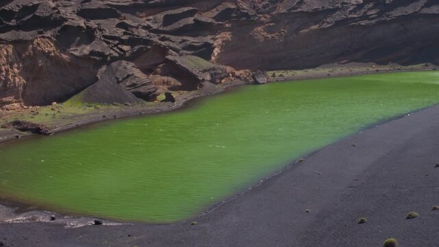 Cinematic wide shot of the emerald green Clicos Lake (Charco de los Clicos) surrounded by black volcanic sand in Lanzarote