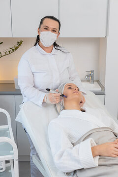 Injection-free mesotherapy or electroporation. Beautician doctor makes client middle-aged woman face therapy in beauty clinic salon. Adult girl skin care anti-age spa procedure. Aesthetic cosmetology.