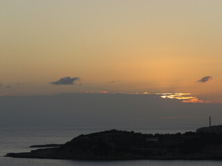 Beautiful Orange Sunrise breaking through clouds over the ocean and silhoutte of rocks with lighthouse