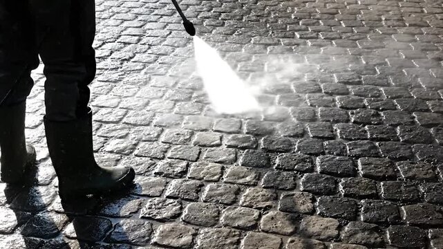 a worker using High pressure water jet cleaning a cobblestone pavement surface outdoors.