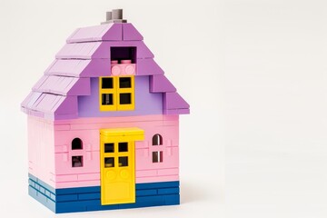 Fototapeta premium Simple pink and purple LEGO house with yellow door on white background, professional photography with space for text