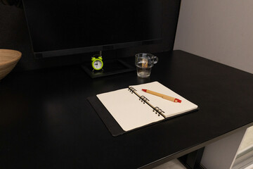 Fototapeta premium Minimalist black desk setup with open notebook, pen, and alarm clock