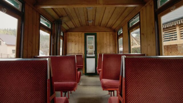 The view shows the interior of a Mocanita train carriage. Red seats line the wooden cabin. Windows provide glimpses of the outside, capturing a historic travel experience.