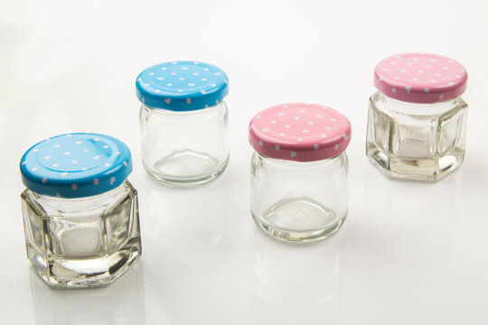 A small hexagonal clear glass jar with a white metal lid, isolated on a white background for food or cosmetics.