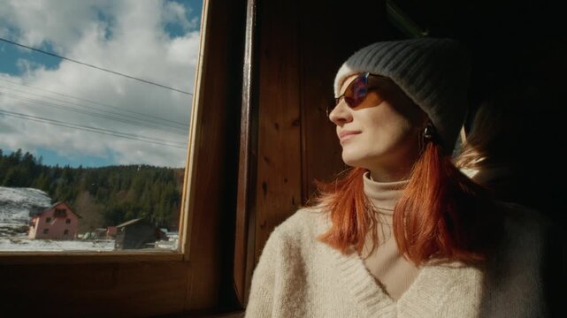 A woman rides an old train in Romania, looking out the window. She watches the beautiful sights as she relaxes and falls asleep during the journey.