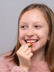 Close-up of a teen girl holding red gummy candy near her lips in studio, sweet snack craving, candy treat, playful lifestyle, sugary temptation.