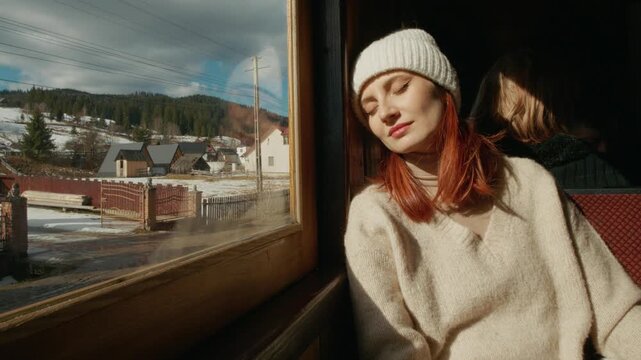 A woman sits by the window of an old train in Romania. She looks out at the countryside and falls asleep while enjoying the journey.