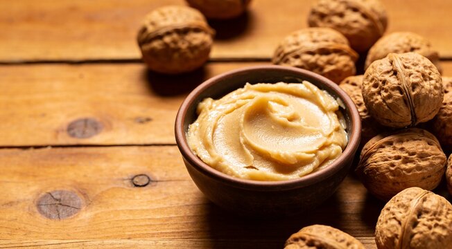 Natural shea butter in bowl and nuts on wooden table, closeup