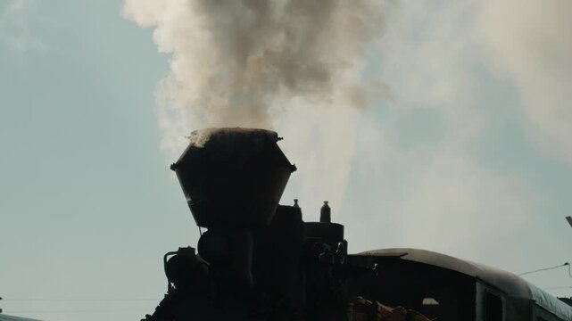 Mocanita steam train stands at the station in Bucovina, Romania, releasing white smoke into the air as it awaits departure. This old locomotive is a sight to see.
