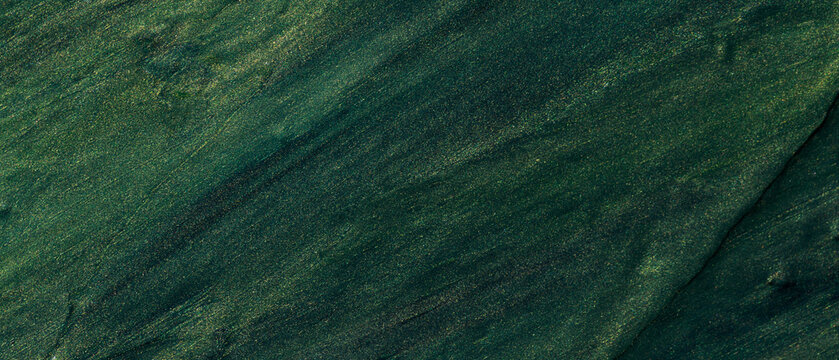 Dark green oil paint brushstrokes with golden glitter particles on textured canvas surface