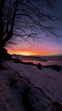 Intense winter sunset on Zugerberg overlooking Lake Zug, snow-covered landscape glowing under a dramatic red and golden evening sky.