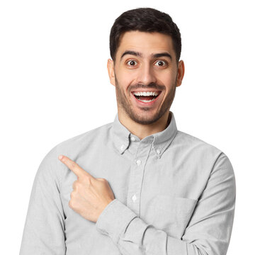Excited young man in grey shirt with wide eyes and big smile pointing sideways, no glasses