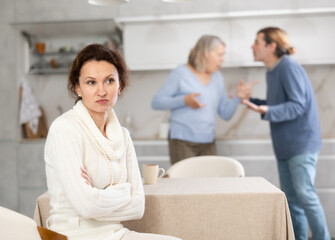 Obraz premium Distressed woman is present during quarrel between her husband and elderly female mom. Mature woman and son-in-law swear and insult each other