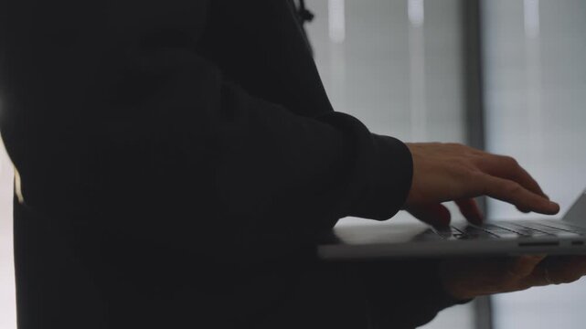 Close up on mysterious male hands typing on laptop computer hacker or spy. Hooded man with black clothes using computer in closed apartment. Dark room in suspicious cyber activity. Espionage or fraud