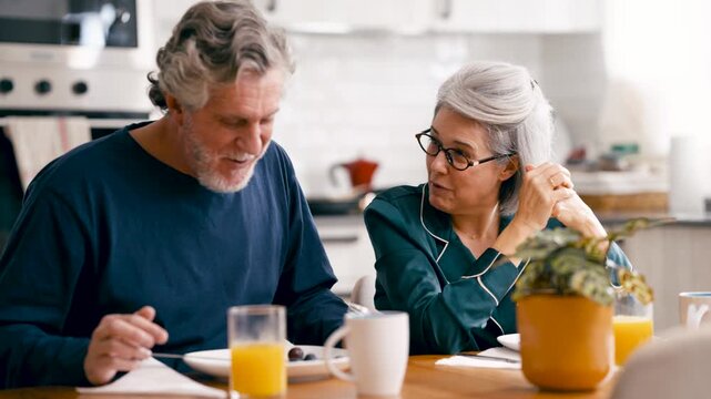 Lovely senior couple in pajamas enjoying a healthy breakfast together. Happy retired man and woman sharing a funny moment at home