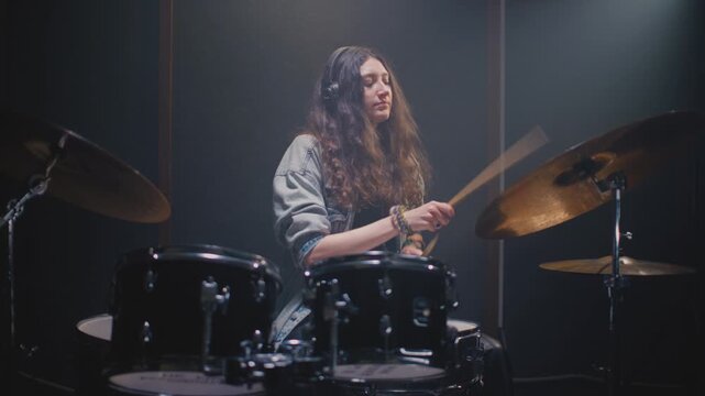 Drummer girl playing drums in music rehearsal studio filled. Rock band music artist learning a drum solo. Young woman with long curly hair, fill or break on drum kit. Female drumming in room