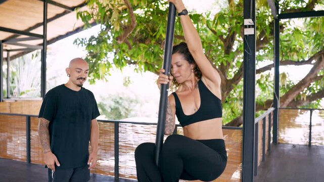 Young woman practicing a pole dancing move under the supervision of her male teacher. Happy student smiling after successfully performing the exercise
