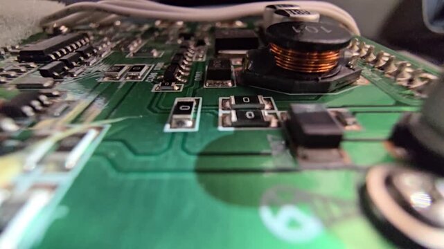Macro steady shot of a high-quality electronic circuit board focusing on a copper wire inductor coil and electrolytic capacitors on a green PCB.