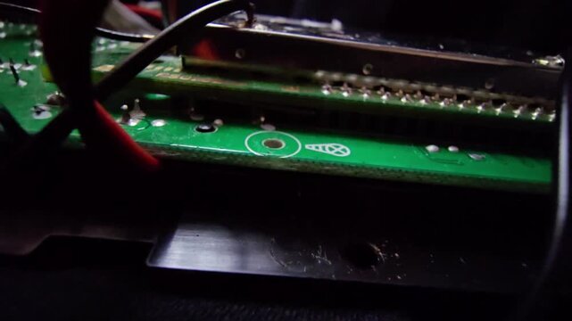 Macro view of a green PCB featuring a metal EMI shield, integrated circuits, and a precision soldered wire connection on a complex electronic motherboard.