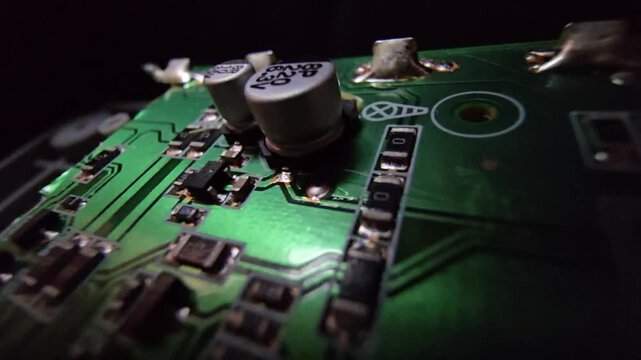 Macro steady shot of a high-quality electronic circuit board focusing on a copper wire inductor coil and electrolytic capacitors on a green PCB.
