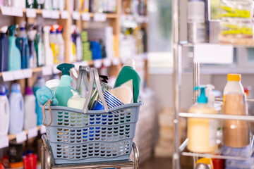 Shopping basket full of essential cleaning products, detergents, sprays, scrubbing tools and personal care products, ideal for home maintenance and hygiene displayed in store for purchase..