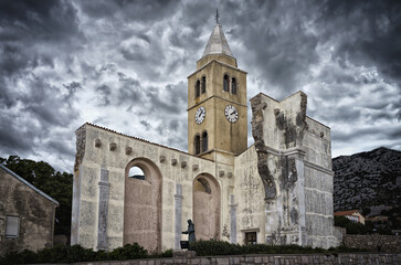 Historic ruins of the St. Charles Borromeo church with its clock tower under a dramatic cloudy sky in Karlobag, Croatia