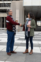 Senior man and woman shaking hands with takeaway cups and scarves on checkerboard plaza © wavebreak3