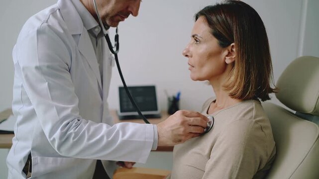 Doctor listening to patients heartbeat with stethoscope during medical examination.