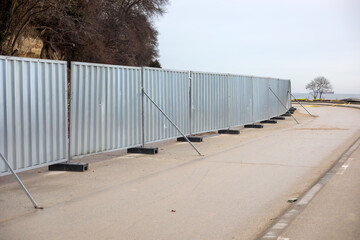 Temporary metal construction fence installed along seaside promenade, safety barrier on empty coastal road with overcast sky