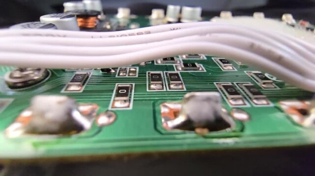 Macro of STM32 microchip on green PCB. Close-up of soldered white wires, electrolytic capacitors, inductors, and SMT components. High-tech circuit board for industrial hardware and engineering.