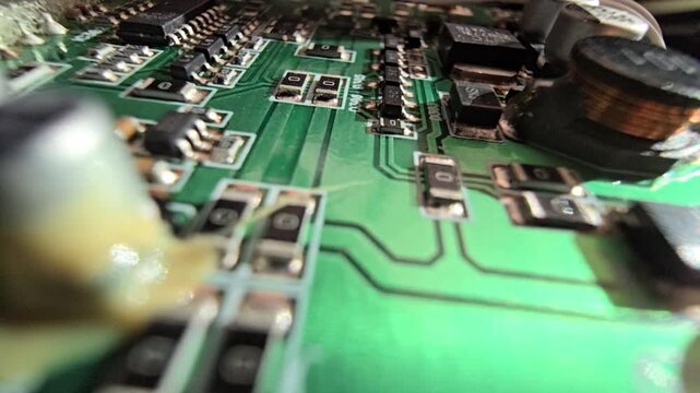 Macro of STM32 microchip on green PCB. Close-up of soldered white wires, electrolytic capacitors, inductors, and SMT components. High-tech circuit board for industrial hardware and engineering.