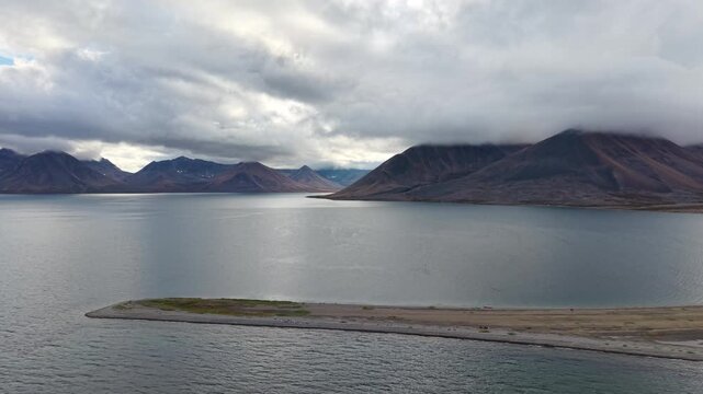 Aerial drone footage follows a sandspit and open water in Rumilet Bay, Chukotka. Smooth tracking right reveals more shoreline and lagoon edge. Early autumn morning under low cloud with remote mood