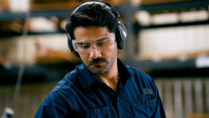 Man focusing on his work, wearing safety glasses and ear muffs for protection in a woodworking workshop © DMegias