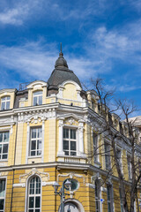 Fototapeta premium a magnificent neo-classical building with a yellow and white facade, featuring a prominent grey dome, ornate window pediments, and white architectural moldings