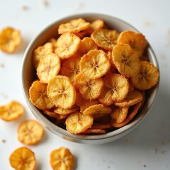 Obraz premium Bowl of dried banana chips on white table. Crispy fruit slices are sweet healthy snack. Perfect for recipes, food blogs, and healthy eating inspiration.