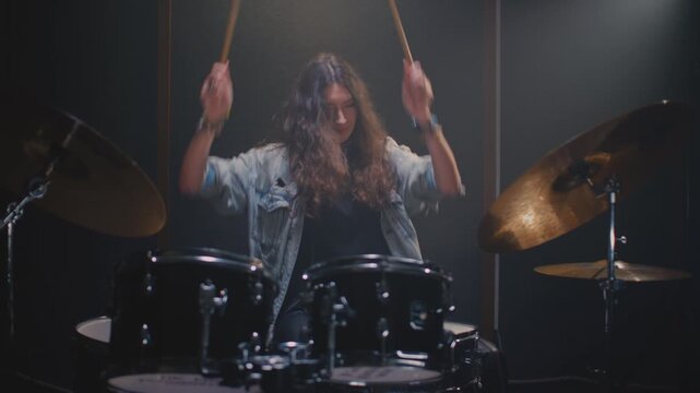 Portrait: female drummer hits drum kit, finishes rehearsal. Music band repetition. Woman with long curly hair, drumming in studio, rock live concert. Modern hobby, art skill. Slow motion