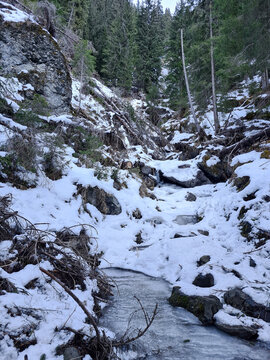 Paesaggio innevato con pini e montagne con ruscello ghiacciato.