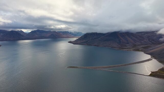 Aerial view across wide bay and long sandspit at Rumilet Bay, Chukotka. Slow pan right follows the shoreline curve and distant ridges. Early autumn morning overcast creates cinematic, moody atmosphere