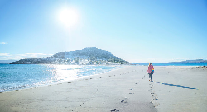 Simos Beach, Elafonisos, Greece: Woman walking on a sandy beach with a hill in the background