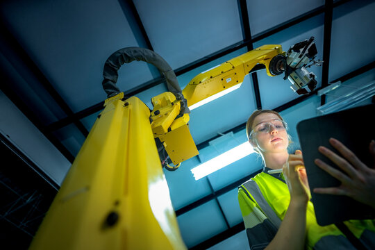 In an Industry 4.0 smart factory, an engineer uses a tablet to run an AI machine vision algorithm on a collaborative robot cobot, optimizing production via a real time digital twin.