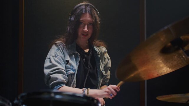 Portrait: female with long curly hair plays the drums. Girl is rehearsing in a studio with drumsticks. Face of a beautiful musician girl, showcasing skill and energy. Underground indie slow motion