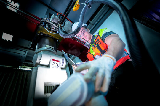 A robotics technician performs a critical repair on the joint of an industrial robotic arm, troubleshooting the servo motor and wiring during a system commissioning or maintenance cycle.