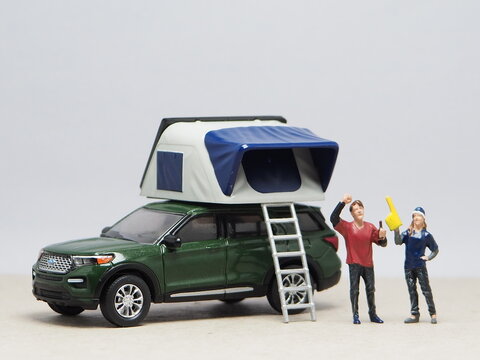 Mini toy of action figure at table with blurred background. Miniature photography concept design. Minifigure of people character with camper van car and roof tent. Holiday and adventure at outdoor.