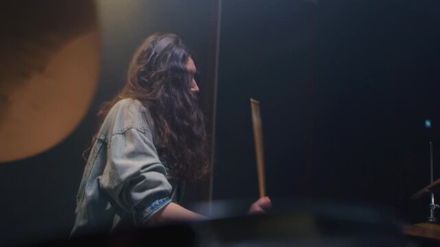 Portrait: female with long curly hair plays the drums. Girl is rehearsing in a studio with drumsticks. Face of a beautiful musician girl, showcasing skill and energy. Underground indie slow motion