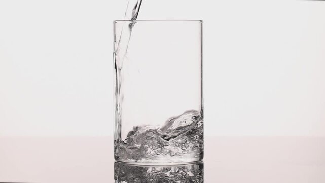 4K slow motion pouring clean drinking water into glass, bubbles forming and splashing, pure hydration and healthy lifestyle concept, studio shot on white background