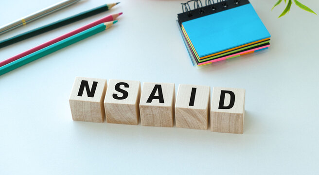 NSAID word made of wooden blocks on white background with pencils and sticky notes.