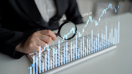 A business professional uses a magnifying glass to examine financial data on a keyboard, with...