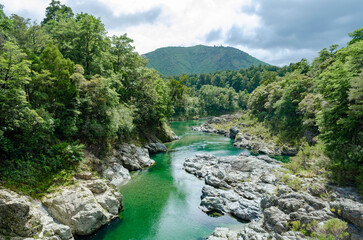 Pelorus River in New Zealand, featuring vibrant turquoise water flowing through a rocky landscape surrounded by lush green forests and hills.